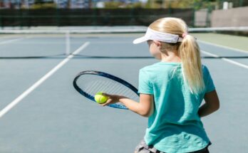 Devojčica sa teniskim reketom i lopticom, na terenu.