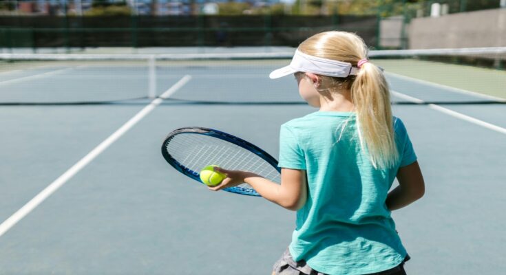 Devojčica sa teniskim reketom i lopticom, na terenu.